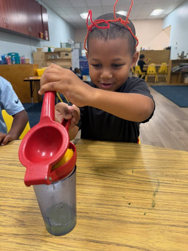 Child juicing an orange during a practical life activity at Sunny West