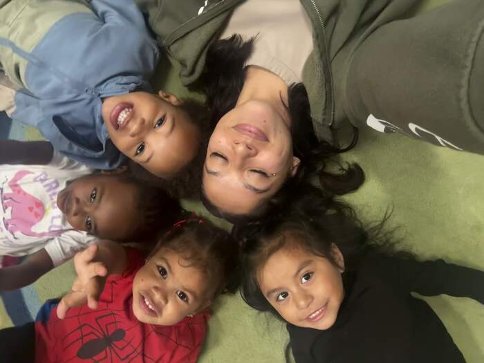 Children and a teacher smiling together in a circle at Sunny West