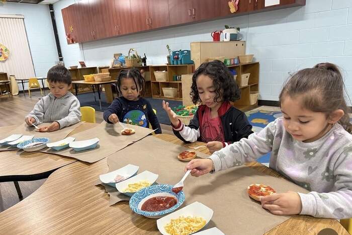 Preschoolers making mini pizzas together at snack time