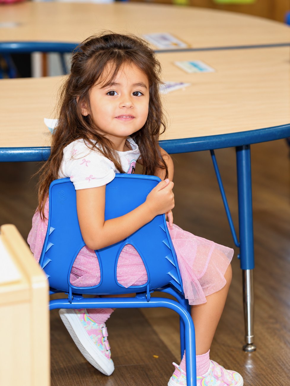 A smiling preschooler sitting at a classroom table at Sunny West